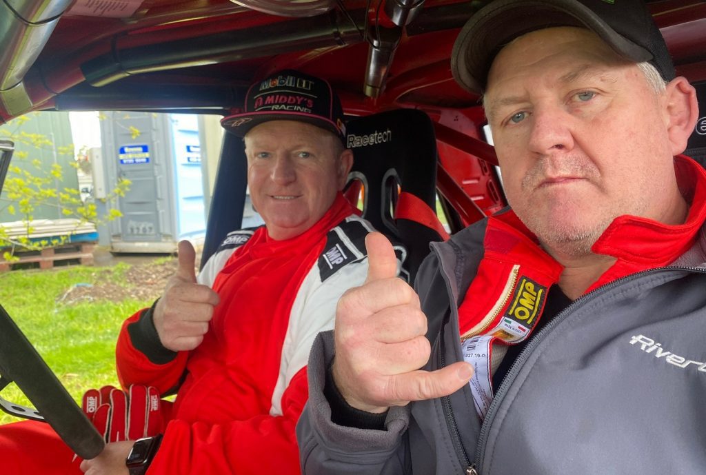 Two men in a rally car wearing racing suits
